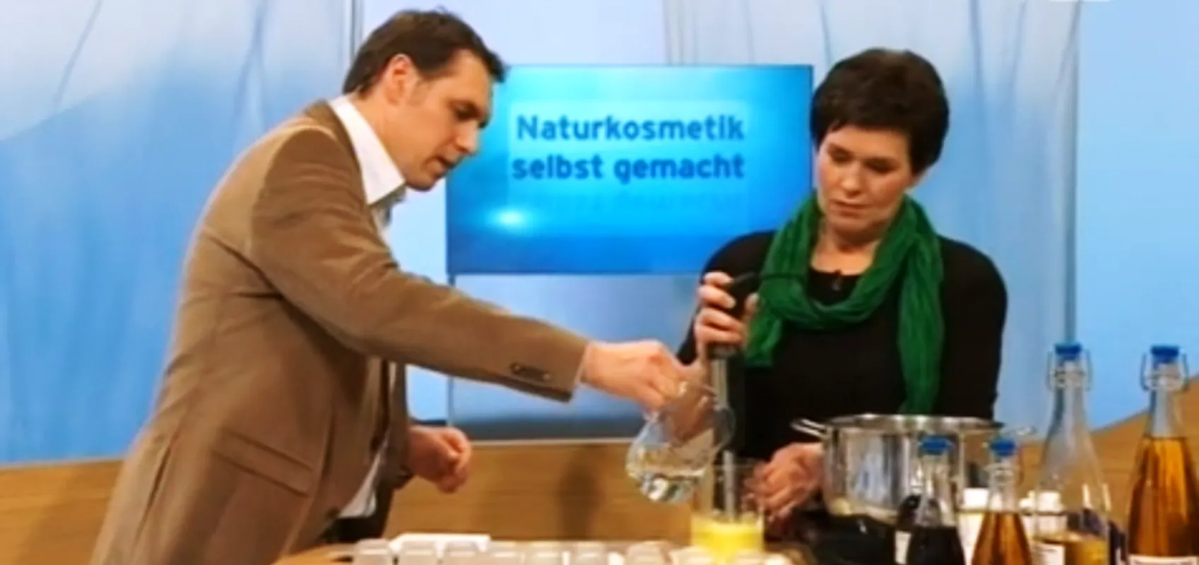 Eine Frau in einer gemütlichen Küche, die mit einem Mörser Zutaten verarbeitet. Im Vordergrund befinden sich handgemachte Naturseifen in Körben.